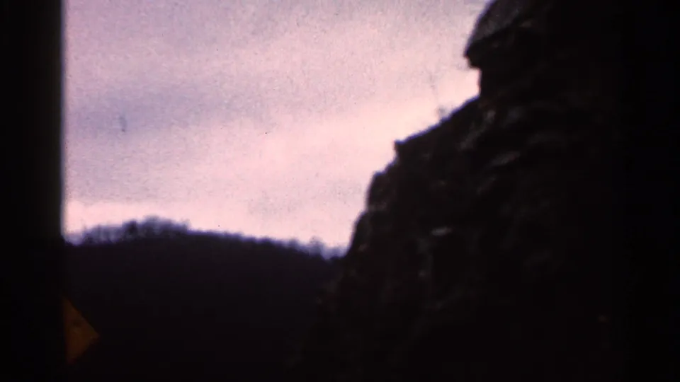 1966 Georgia home-movie frame of a muted mountain ridge and roadside rock face viewed through a moving car window.