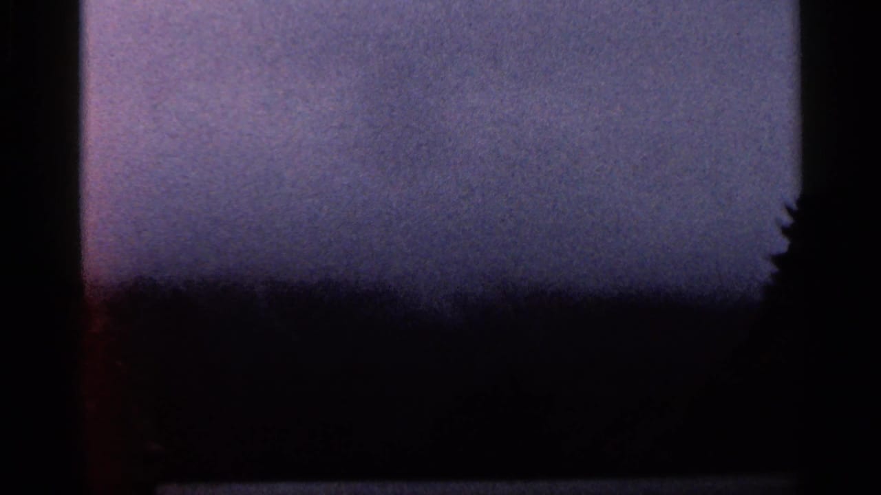 1966 Georgia 8mm view of a hazy mountain distance, dark tree line, and vehicle-window edge during road travel.