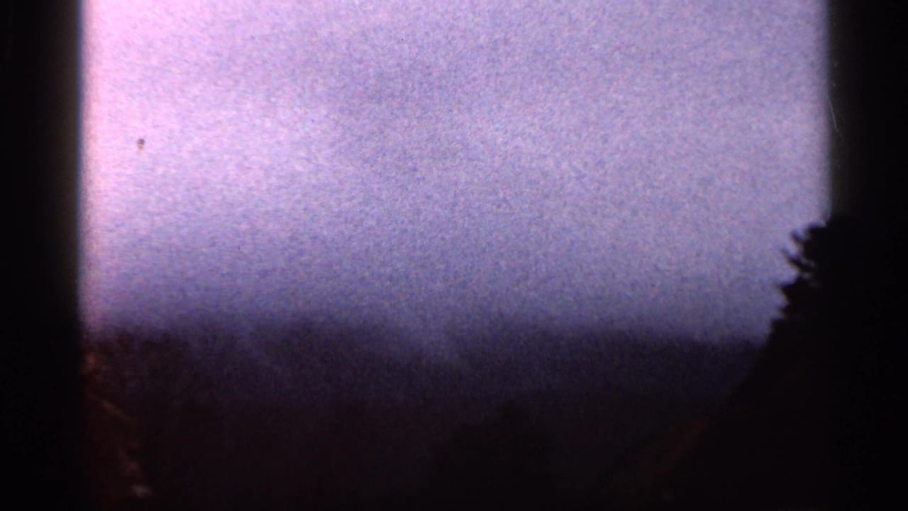 1966 Georgia home-movie frame showing pale mist above a distant ridge, with roadside rock barely visible at the right edge.
