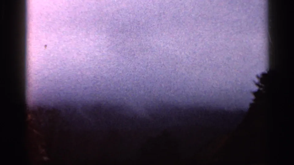 1966 Georgia home-movie frame showing pale mist above a distant ridge, with roadside rock barely visible at the right edge.