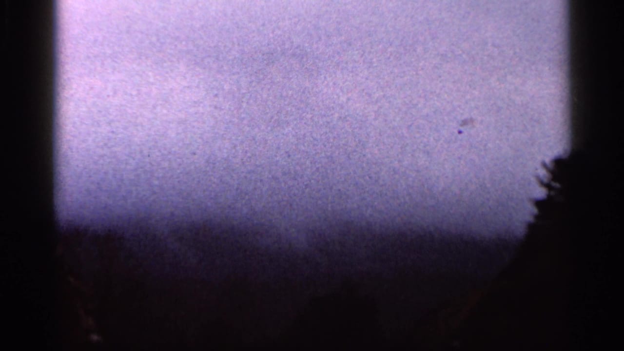 1966 Georgia 8mm frame showing a purple-gray overcast sky and dark tree silhouettes, partly obscured by vertical black edges.