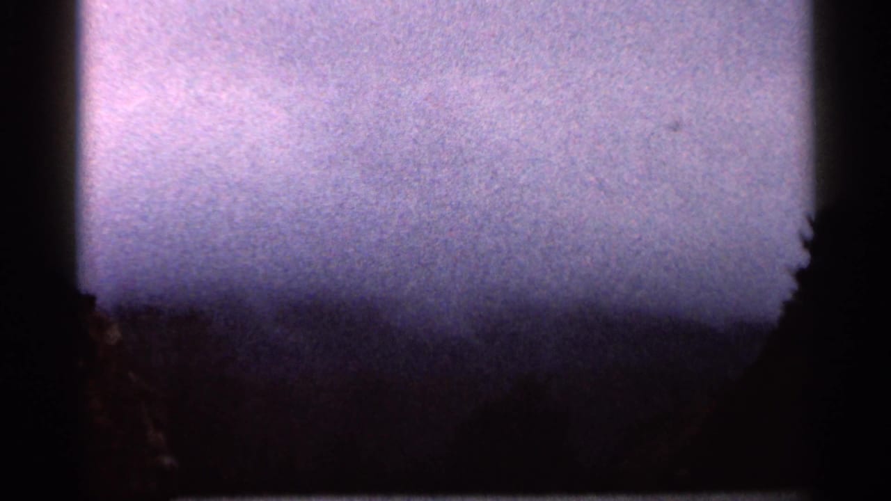 1966 Georgia 8mm view of a muted cloudy sky and dark wooded horizon, with heavy grain and black frame edges.