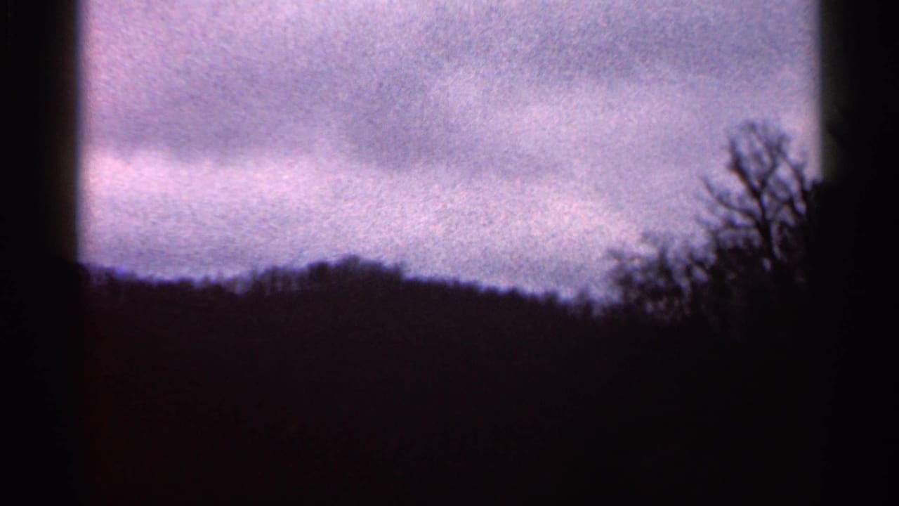 1966 Georgia 8mm frame with layered clouds, a low dark treeline, and bare branch silhouettes along the right side.