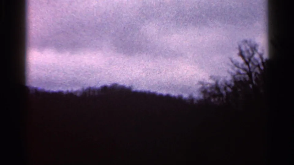 1966 Georgia 8mm frame with layered clouds, a low dark treeline, and bare branch silhouettes along the right side.