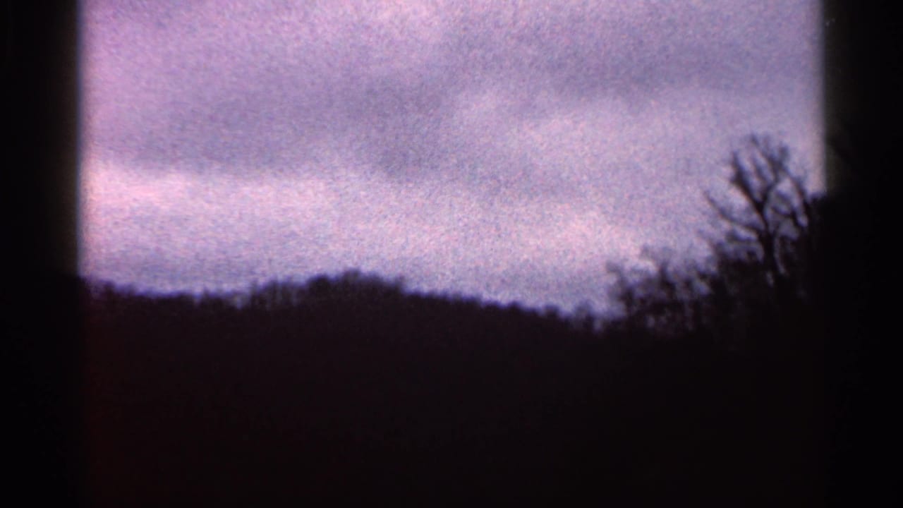 1966 Georgia 8mm view of purple-gray clouds above a shadowed wooded horizon and bare trees at the right edge.