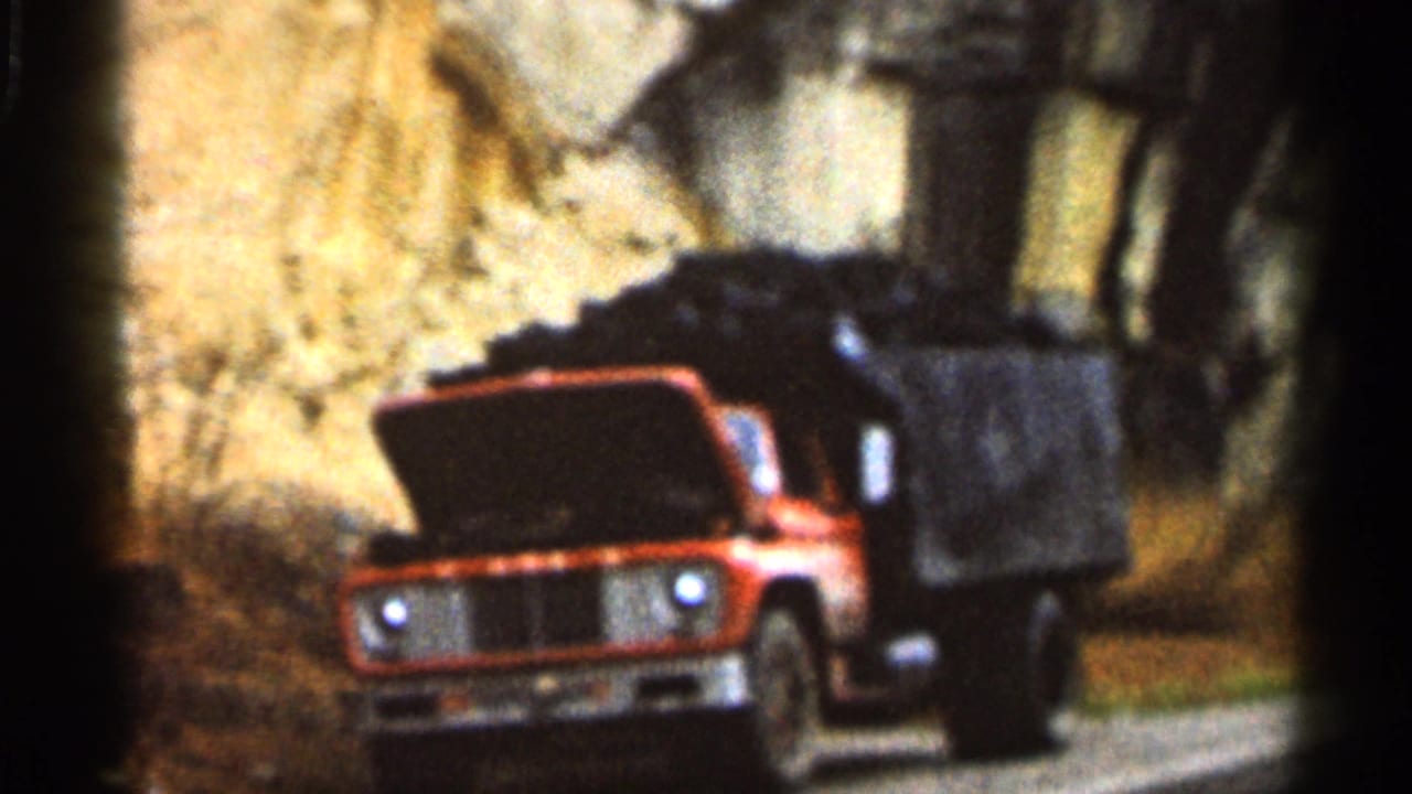 1966 Georgia home-movie frame of a red truck stopped beside a rocky roadside, its hood open in a wooded area.