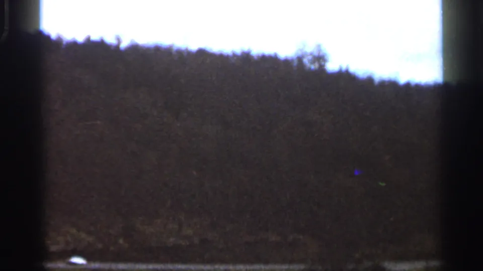 End frame of a 1966 Georgia rural road view, showing a wooded hill, bright sky, and dark film borders.