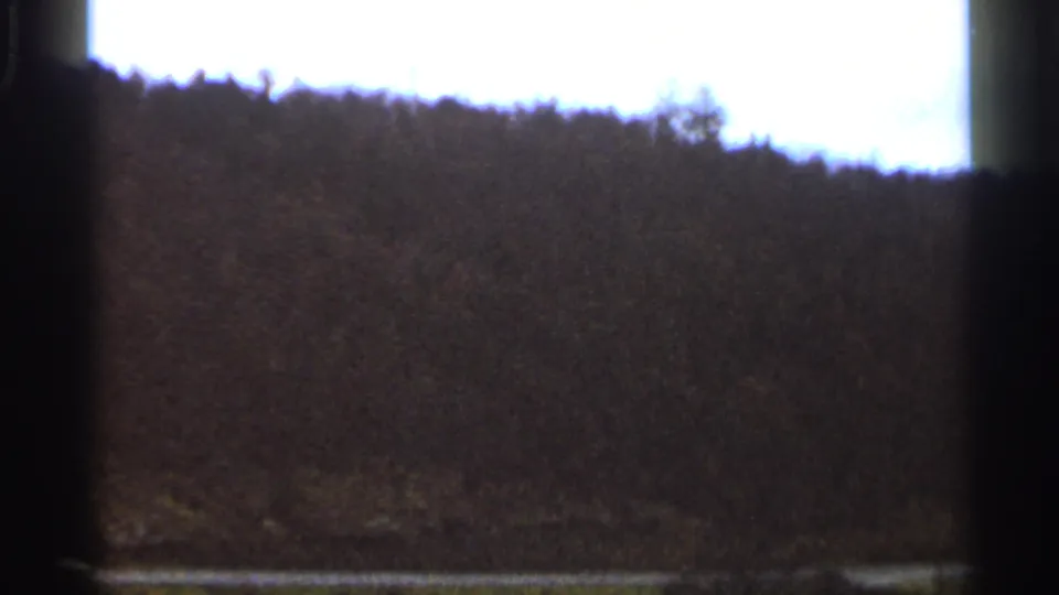 1966 Georgia 8mm frame showing a dark wooded ridgeline beneath an overexposed sky with visible film edge shadows.