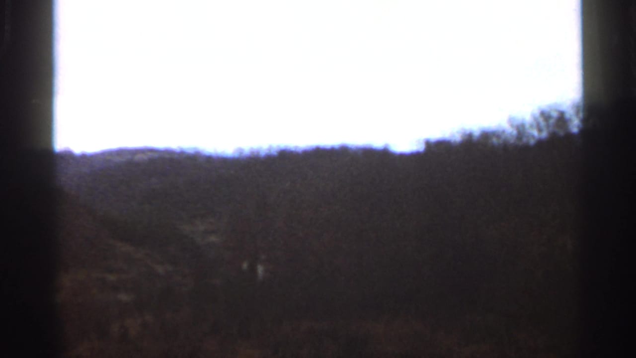 1966 Georgia 8mm landscape frame with wooded hills, pale sky, and a dark vertical obstruction near the center.