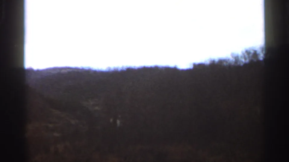1966 Georgia 8mm landscape frame with wooded hills, pale sky, and a dark vertical obstruction near the center.