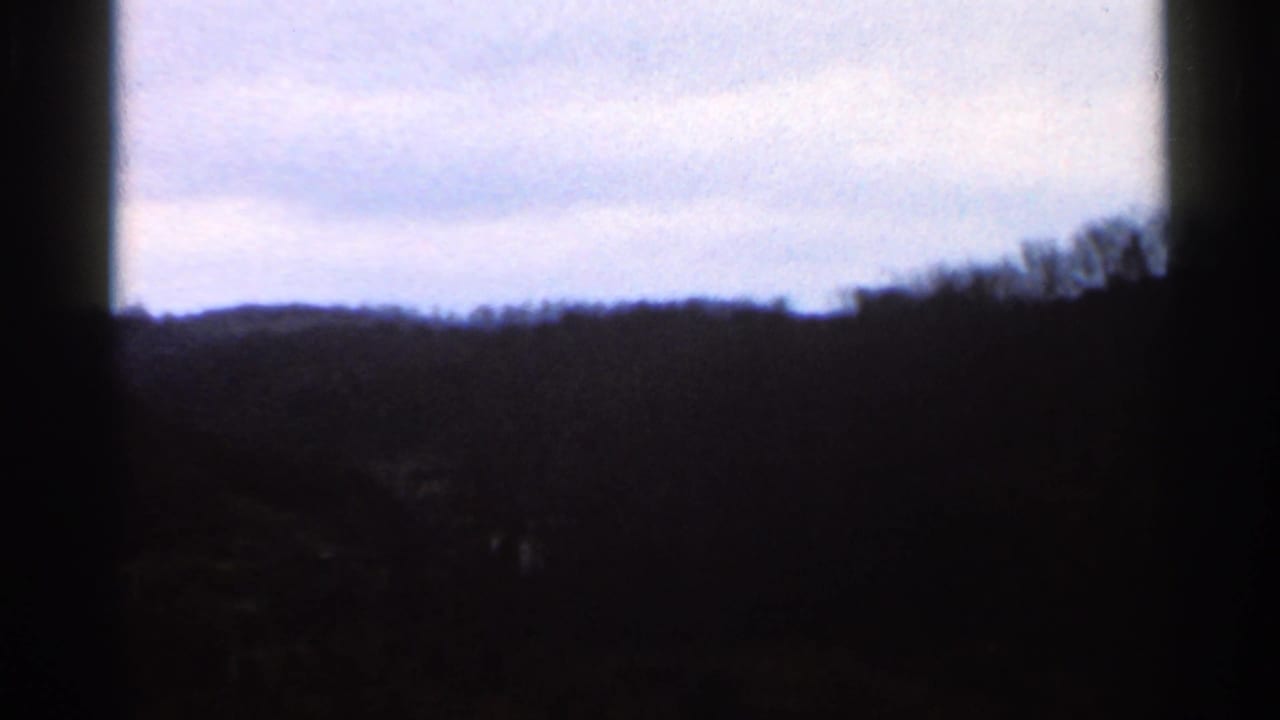 1966 Georgia 8mm frame showing a low, dark treeline under pale blue sky with pronounced underexposure and edge shadow.