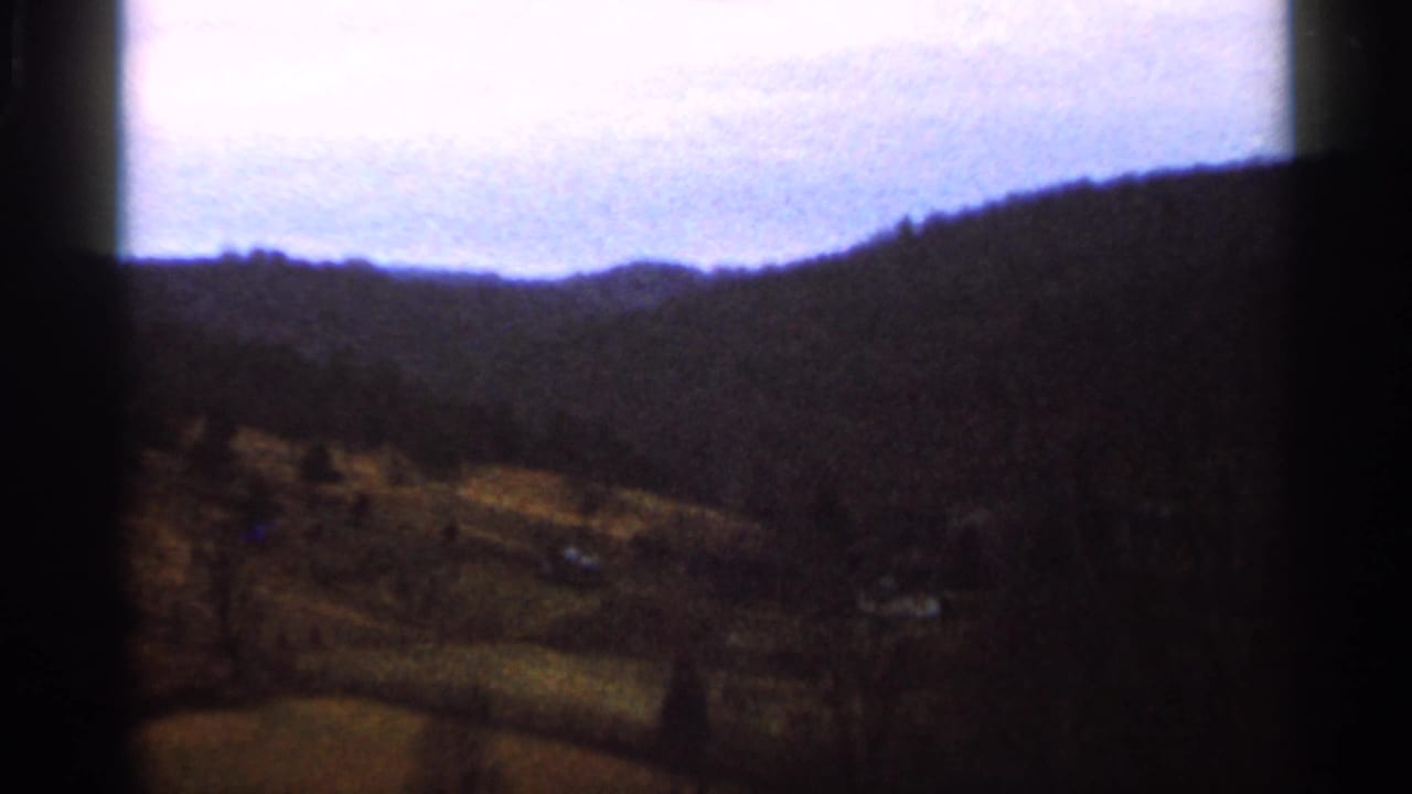 1966 Georgia 8mm frame showing rolling rural farmland, wooded hills, and a pale sky with dark frame-edge vignetting.