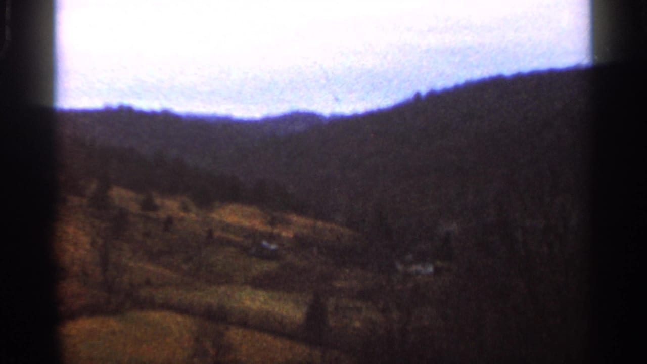 Distant wooded hills and valley fields under a pale sky, seen through dark film gate edges.
