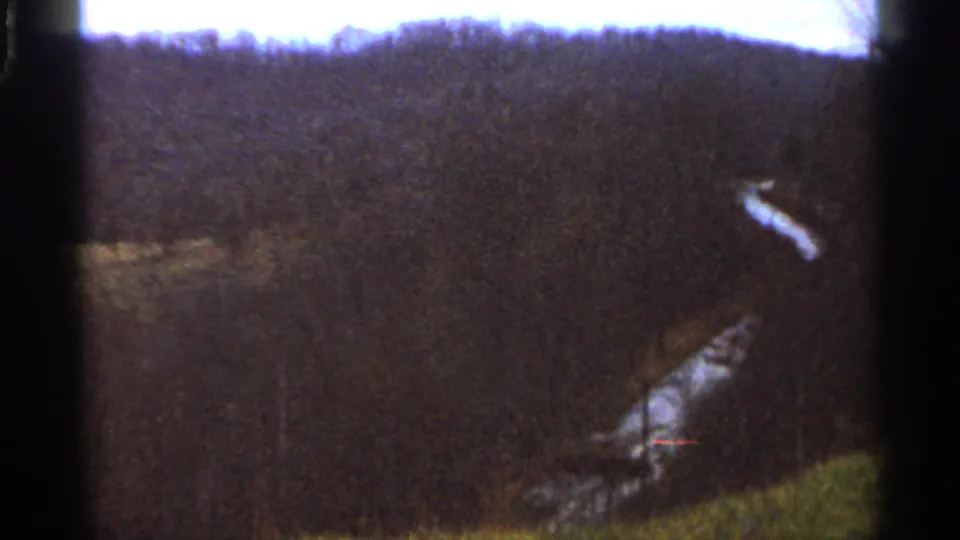 1966 Georgia countryside frame showing a dark forested slope and a pale winding line, possibly a stream or narrow road, near the lower valley.