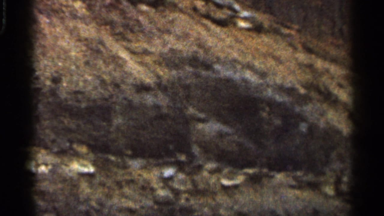 1966 Georgia 8mm frame showing rocky, fire-scarred ground with ash and dark burned patches in close view.