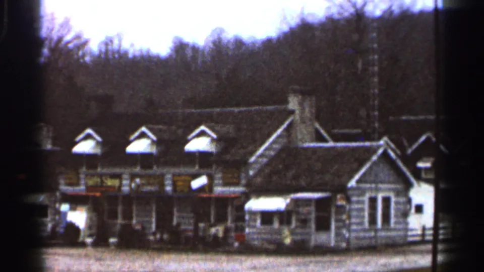 Home-movie view of a Georgia roadside gift shop or restaurant building, with dormers, signs, a small awning, and wooded hills beyond.