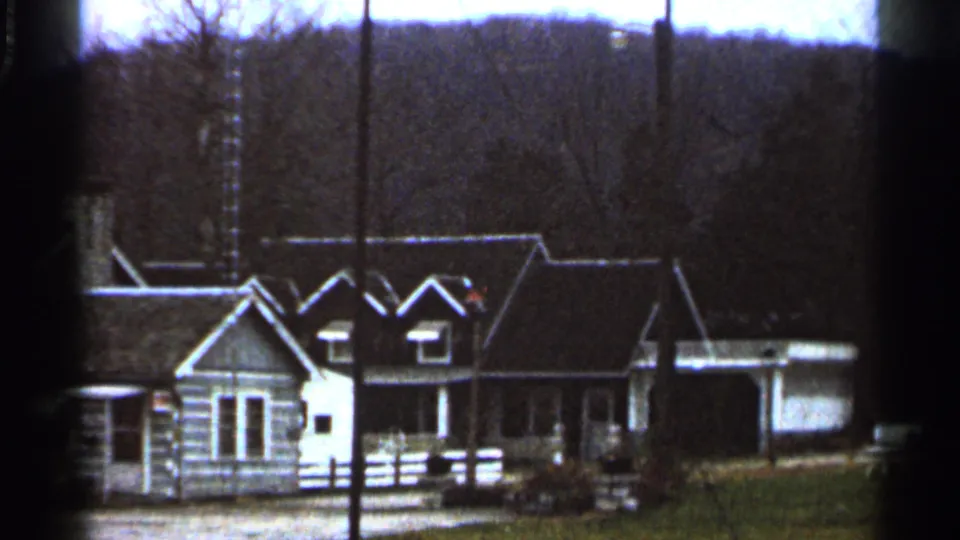1966 Georgia frame showing the gabled end of a rustic roadside building, nearby shelter-like structure, fence, gravel lot, and wooded slope.