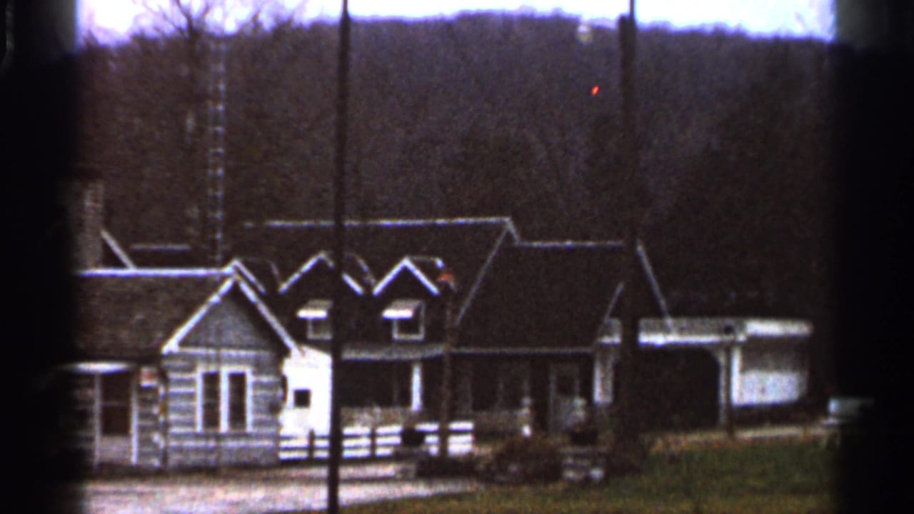 1966 8mm frame showing rustic log-style cabins with white trim, lawn, bare trees, and distant hills in Georgia.