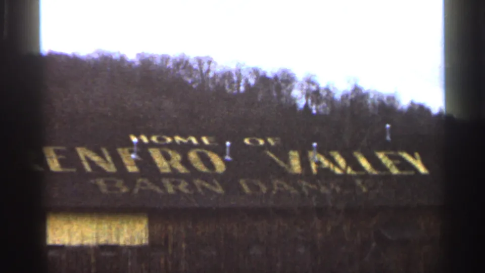 1966 8mm frame with the roof sign Home of Renfro Valley Barn Dance visible against bare trees and hillside.