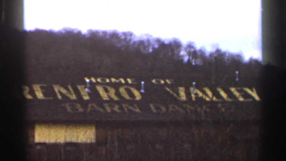 1966 8mm frame showing the Renfro Valley Barn Dance roof lettering, a small window, bare trees, and a wooded hillside.