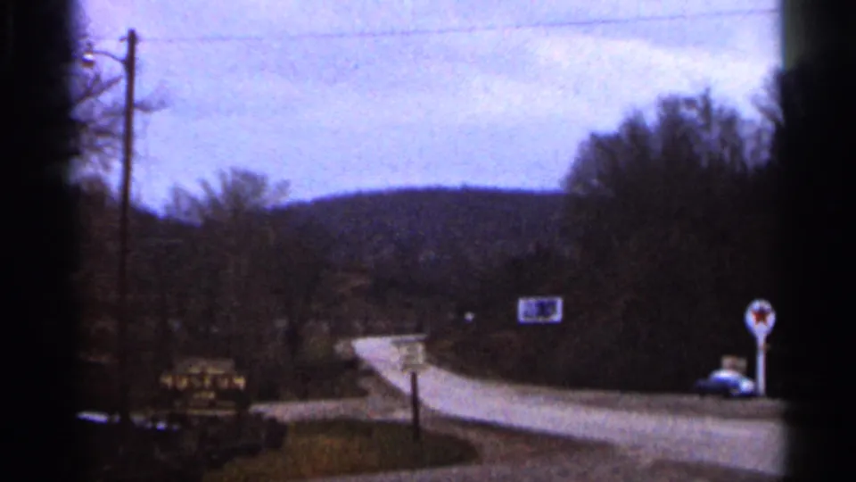 1966 Georgia home-movie view of a curving rural road, roadside signs, leafless trees, and a parked blue car.