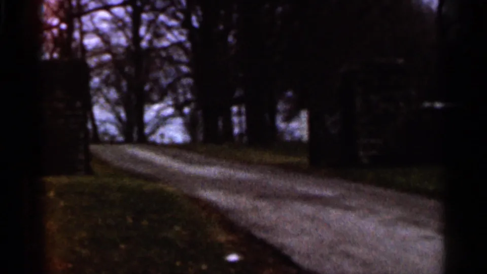 1966 Georgia 8mm frame with a shadowed road, bare trees, grass verge, and a dark stone or brick roadside structure.