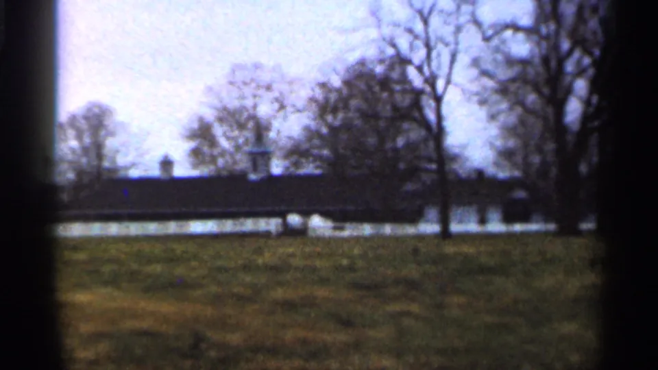 1966 Georgia 8mm frame with a distant low building, white fence, winterlike trees, and foreground grass.