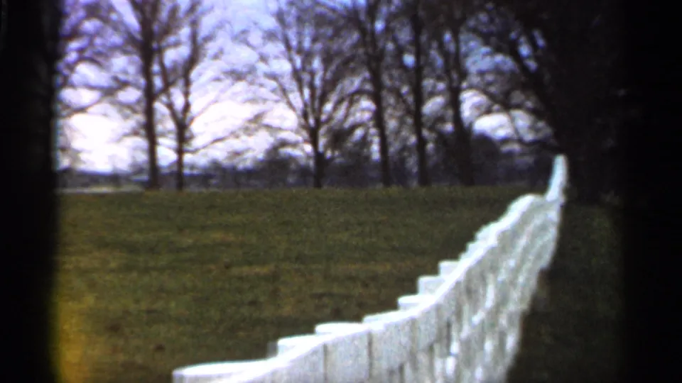 The white fence continues through a grassy Georgia landscape, with bare trees and soft 8mm grain visible in the frame.