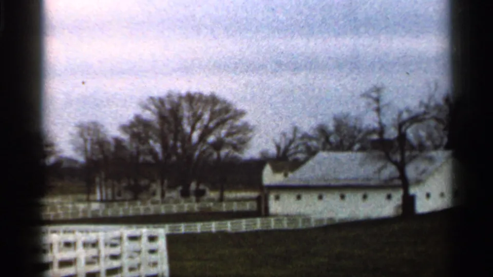 1966 Georgia home-movie frame of a white rural building and fence line, with bare trees and visible 8mm gate edge.