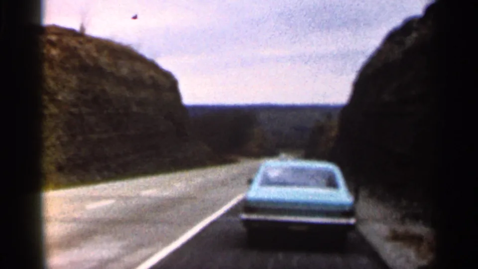 1966 Georgia 8mm frame showing a blue car from behind on a two-lane road passing between rocky hills.