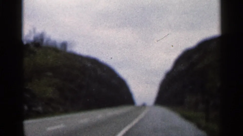 Final 1966 Georgia 8mm frame of an empty two-lane road bending through rocky hills beneath an overcast sky.