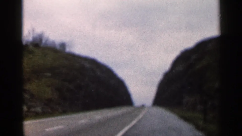 1966 Georgia 8mm road-trip view of a two-lane road passing between rocky, wooded hills under a washed-out sky.