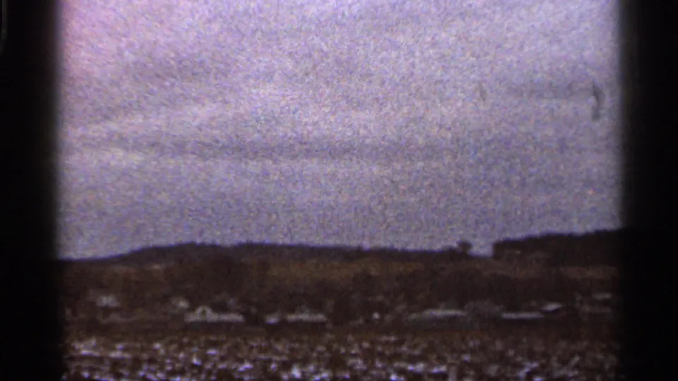 Grainy 1966 Georgia view across open land toward distant low buildings beneath a cloudy sky.
