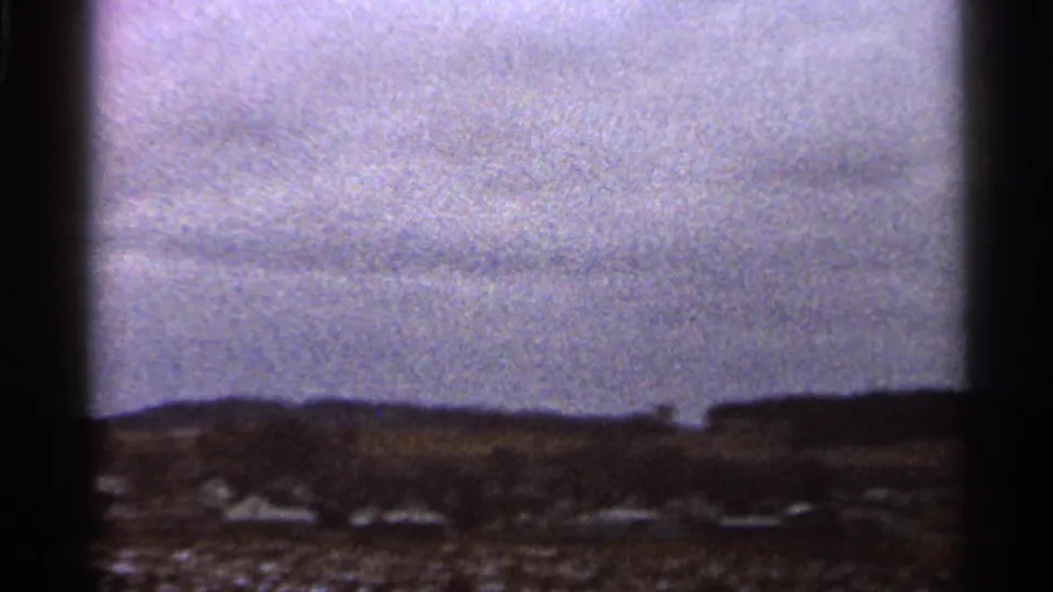 Soft 8mm view of open Georgia terrain with distant structures, low hills, and a bright cloudy sky.