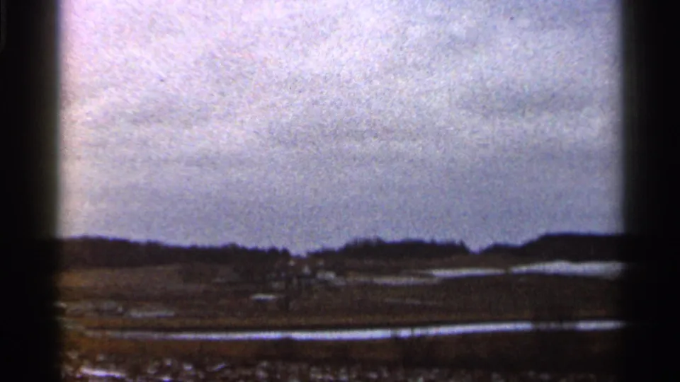 1966 Georgia 8mm frame showing a gray sky over open rural land, distant trees, and bright reflective patches near the ground.