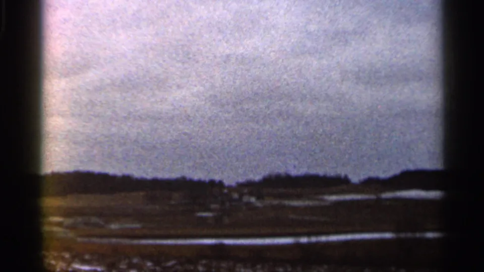 1966 Georgia home-movie view of open countryside, low distant hills, and reflective wet areas beneath a muted cloudy sky.