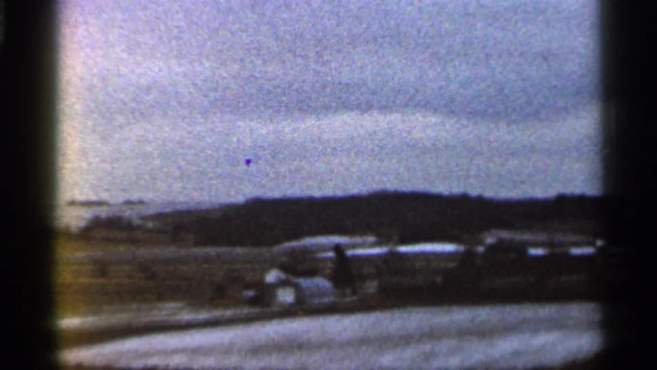 Vintage vehicles stand near open Georgia countryside, with dark 8mm frame edges and visible film grain.