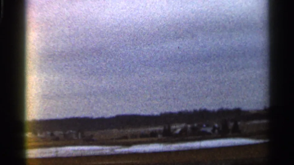 Wide 1966 Georgia home-movie view of distant vehicles and small figures across open ground below hills.