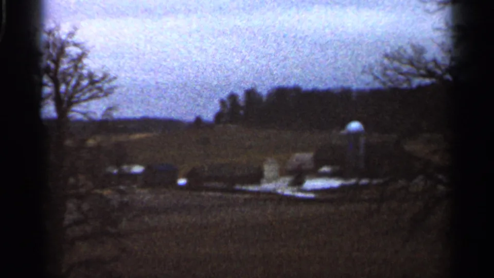 Rural Georgia winter view with bare trees, patchy snow, a small outbuilding-like form, open ground, and soft grain from 8mm film.