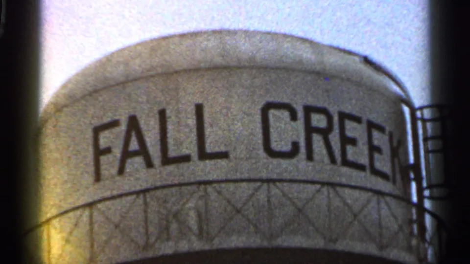 1966 Georgia 8mm frame of the FALL CREEK water tower with railings, support structure, grain, and a warm lens flare.