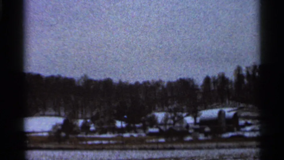 8mm home-movie view of a rural Georgia farmstead in winter, with snow on the ground and barns set below a wooded rise.