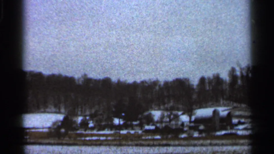 Georgia 1966 8mm frame showing a quiet snow-covered farm landscape with bare trees, low buildings, and a washed winter sky.