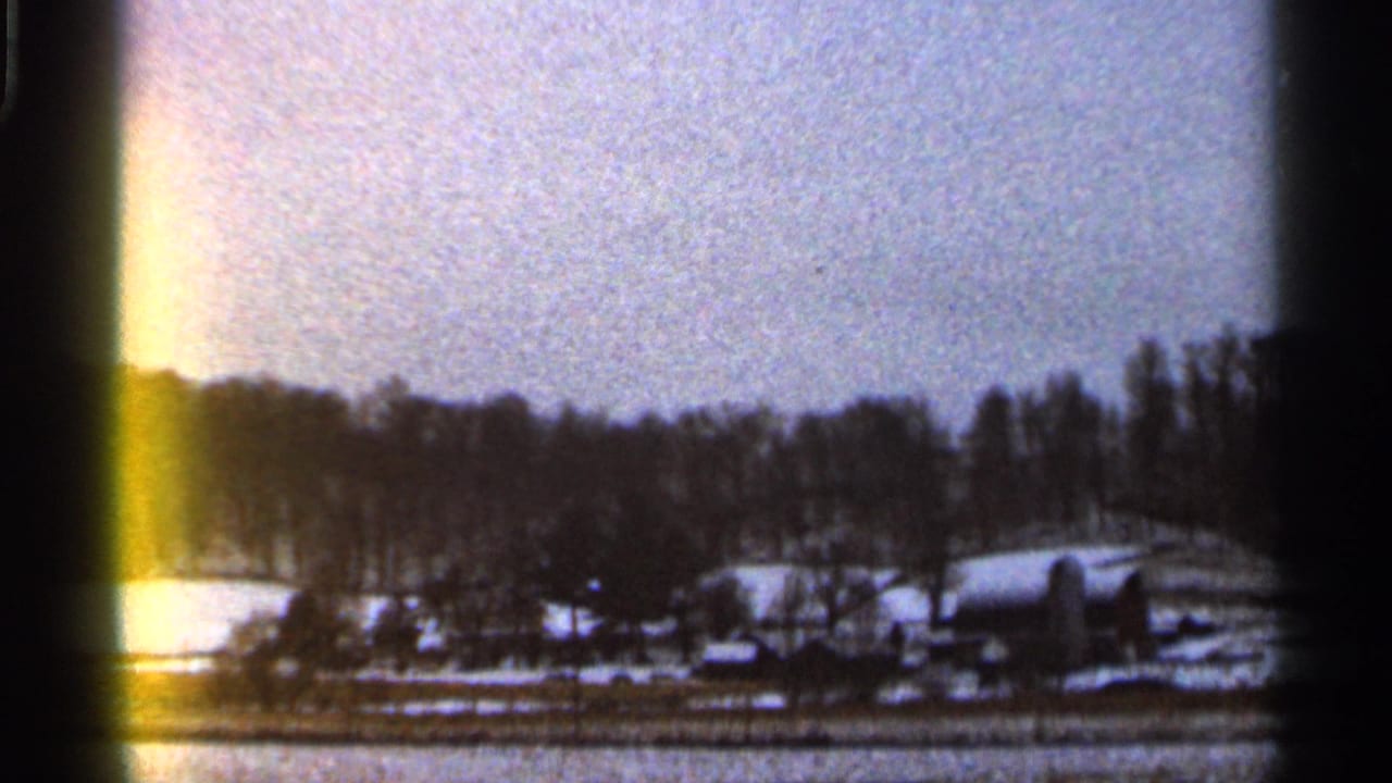 1966 Georgia home-movie frame showing snow-covered fields, bare winter trees, and distant rural buildings with visible film gate edges.
