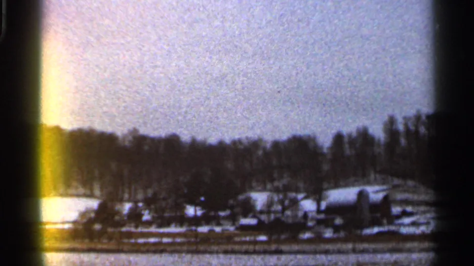 1966 Georgia home-movie frame showing snow-covered fields, bare winter trees, and distant rural buildings with visible film gate edges.