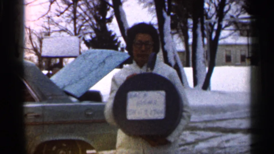 The final frame centers the woman holding the round case, with the car, raised hood, snow, bare trees, and houses visible in the background.