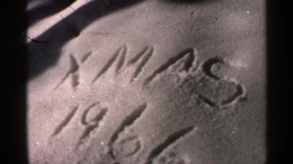 1966 Georgia home-movie frame showing “XMAS 1966” written on a textured surface, with film grain, shadows, and dark frame edges.