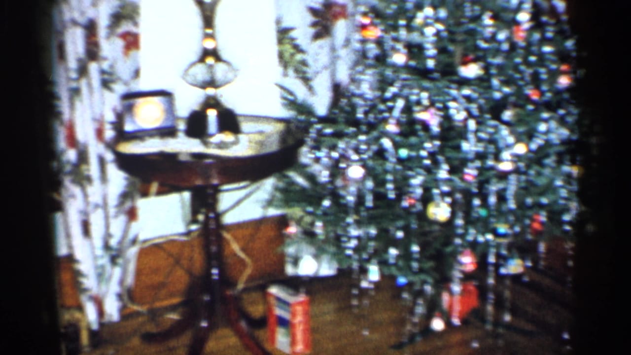 Christmas tree, side table, lamp, clock, curtains, and gifts in a living room.