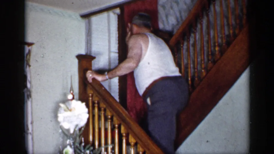 The man continues up the staircase inside a private New York home, with the Christmas tree partly visible below.