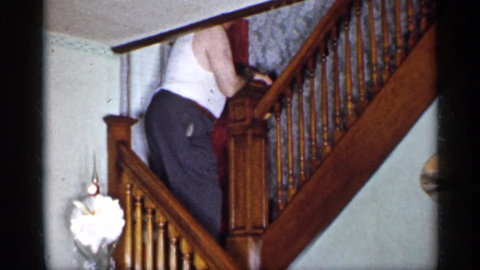 A 1955 home-movie frame shows the man from behind on the stairs, with tinsel and ornaments visible near the base.