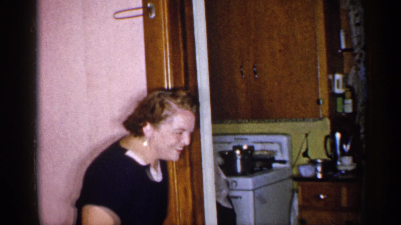 Woman smiles beside a doorway, with a white stove, cabinets, and cookware visible in the kitchen.